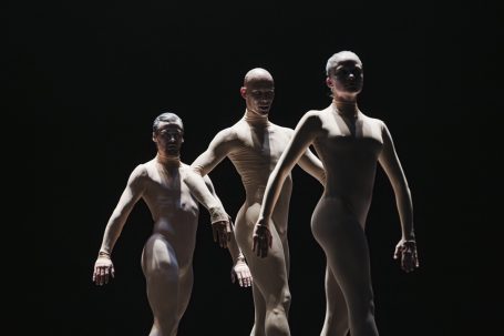 Corps de Walk - Staatstheater Wiesbaden Drei stilisierte, menschliche Figuren stehen in einer dunklen Umgebung.