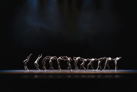 Corps de Walk - Staatstheater Wiesbaden Eine Gruppe von Tänzern in synchronen, dynamischen Posen auf einer dunklen Bühne.