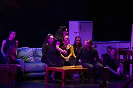 Castor et Pollux - Salzburger Festspiele Gruppe von Personen auf einer Bühne, gekleidet in Schwarz, versammelt um einen Holztisch.